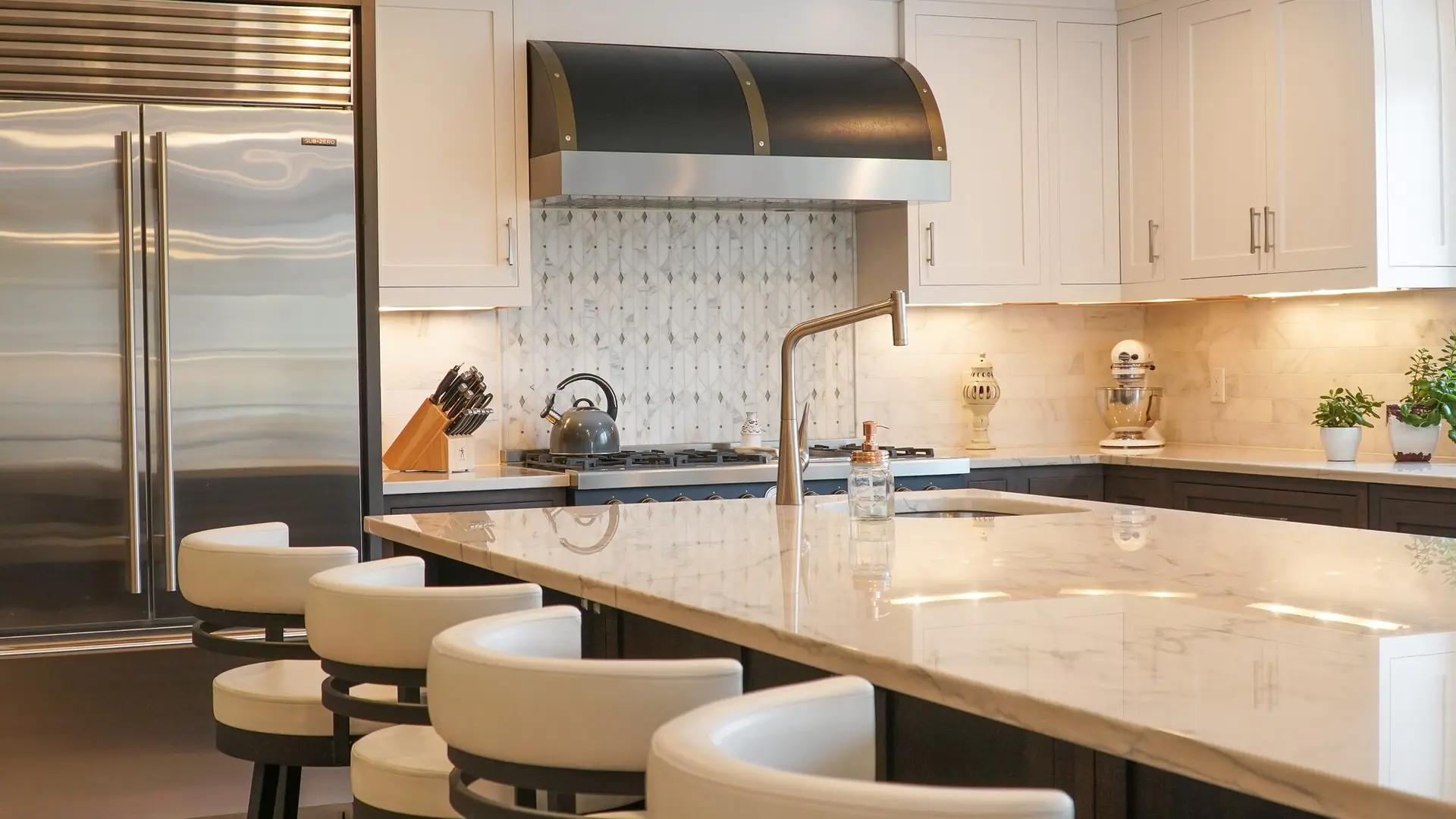 A custom kitchen with a marble waterfall island, white cabinetry and a brass-trimmed range hood