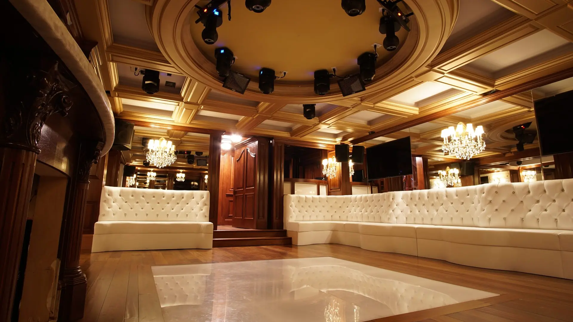 A finished basement lounge with a coffered ceiling, chandeliers and tufted banquette seating